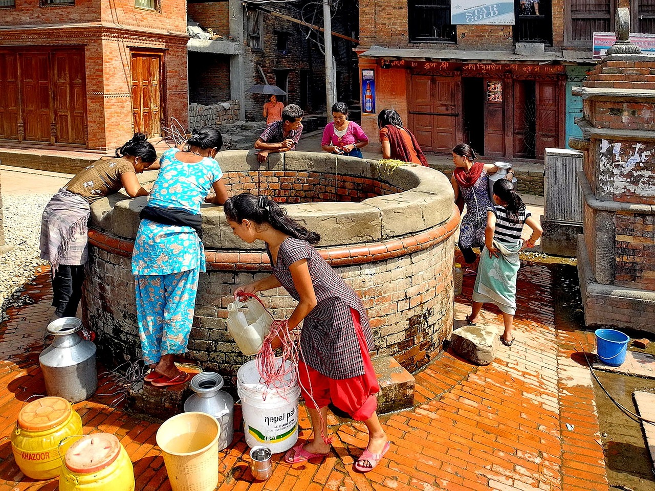 Women taking water out of a well in the middle of a neighborhood | volunteer in nepal 